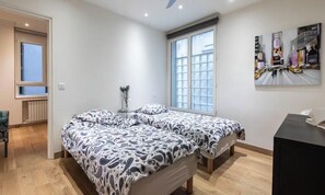 A bedroom with a bed, a desk, a chair, a window, and a painting on the wall.