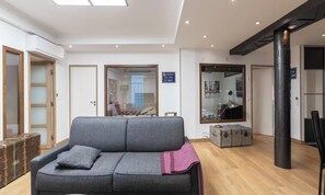 Una sala de estar moderna con un sofá gris, piso de madera, un espejo grande y una maleta.