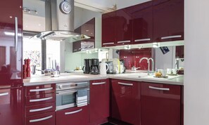 Una cocina moderna con electrodomésticos de acero inoxidable, armarios rojos y un reloj visible en la pared.