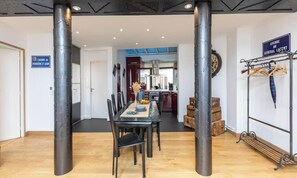Un espace repas avec une table et des chaises, une cuisine en arrière-plan et une structure métallique avec des valises.