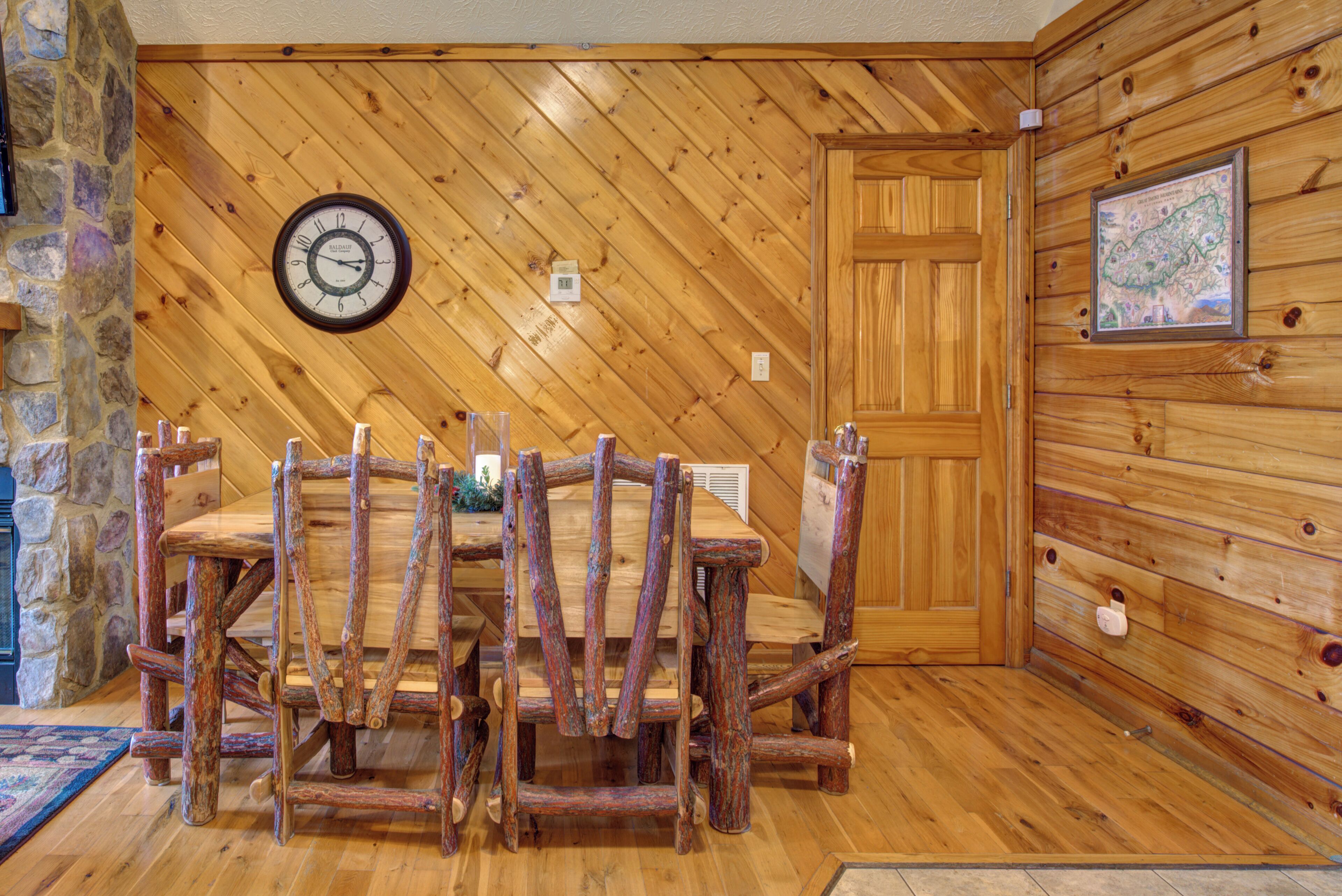 Un coin repas en bois, avec une table et des chaises en bois d’aspect rustique, une horloge murale et une carte encadrée.