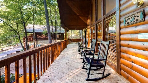 A wooden porch with rocking chairs, a wooden railing, and a sign that reads "Welcome".