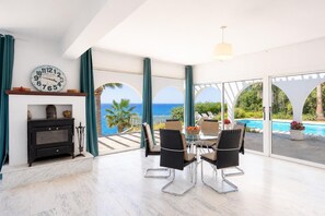 Uma sala de estar moderna com lareira, mesa de jantar e cadeiras, grandes janelas com vista para o mar.