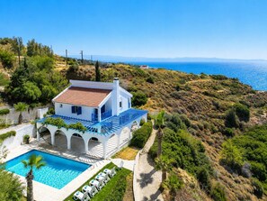 Una villa blanca con techo de tejas rojas, una piscina y vista al mar.