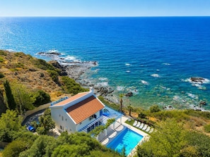A coastal property with a swimming pool, a terrace with lounge chairs, and a view of the sea.