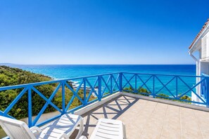 A balcony with a view of the ocean, white lounge chairs, and a blue railing.