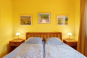 Een tweepersoonsbed met gestreept beddengoed, twee nachtkastjes met lampen, en drie ingelijste schilderijen aan de muur.