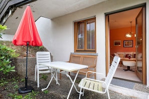 Een terras met een tafel, twee stoelen en een rode parasol.