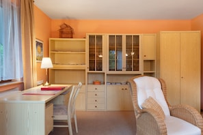 Een kamer met een bureau, stoel, planken en een rieten stoel.