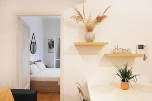 Una camera da letto con un letto, un comodino, una sedia, uno scaffale con una pianta e una mensola a parete con un oggetto decorativo e un cartello.