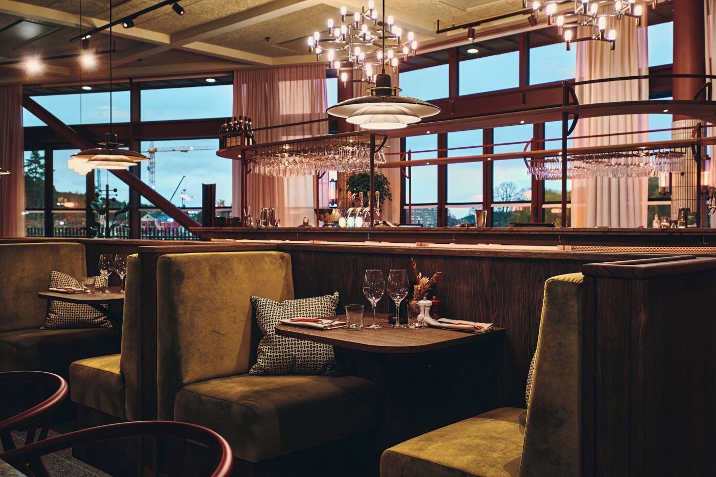 Un restaurante con asientos tipo cabina, una zona de bar con una estantería para vinos y grandes ventanales con vistas al exterior.