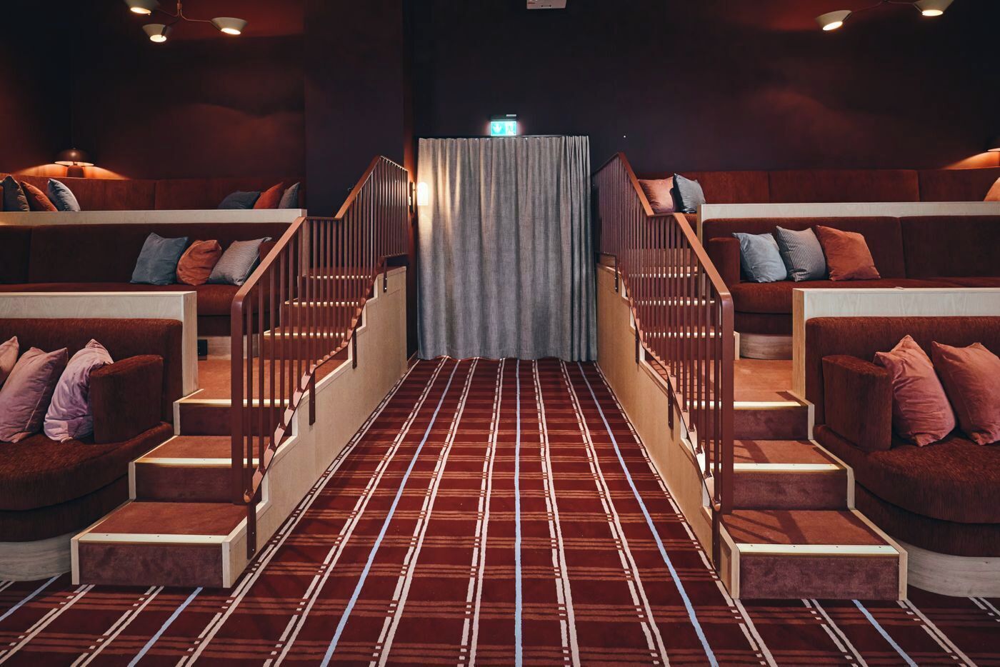 A theater with a red carpeted aisle, wooden steps, and cushioned seating on either side.