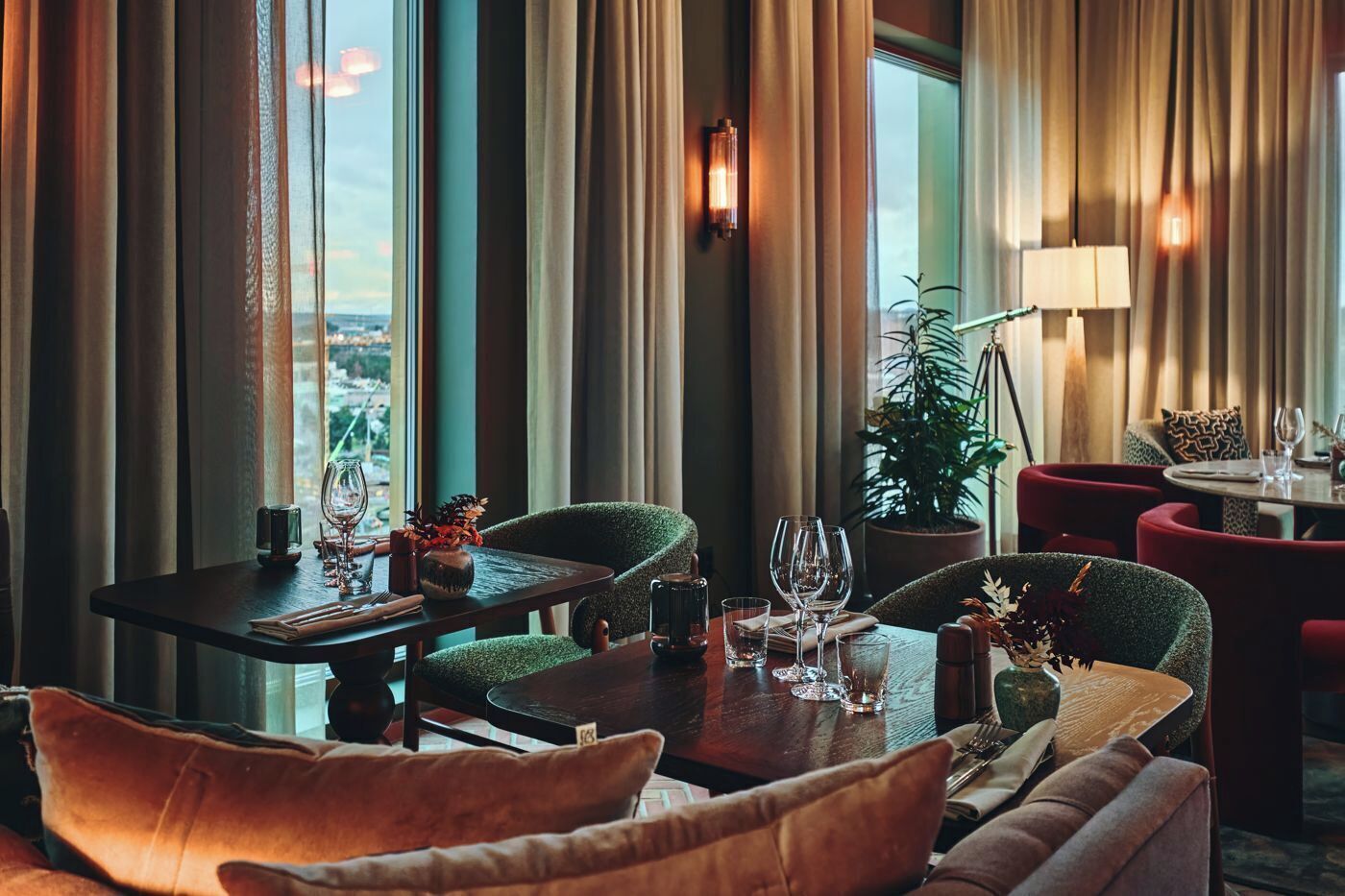 A restaurant with a view of the city, large windows, and modern furnishings.