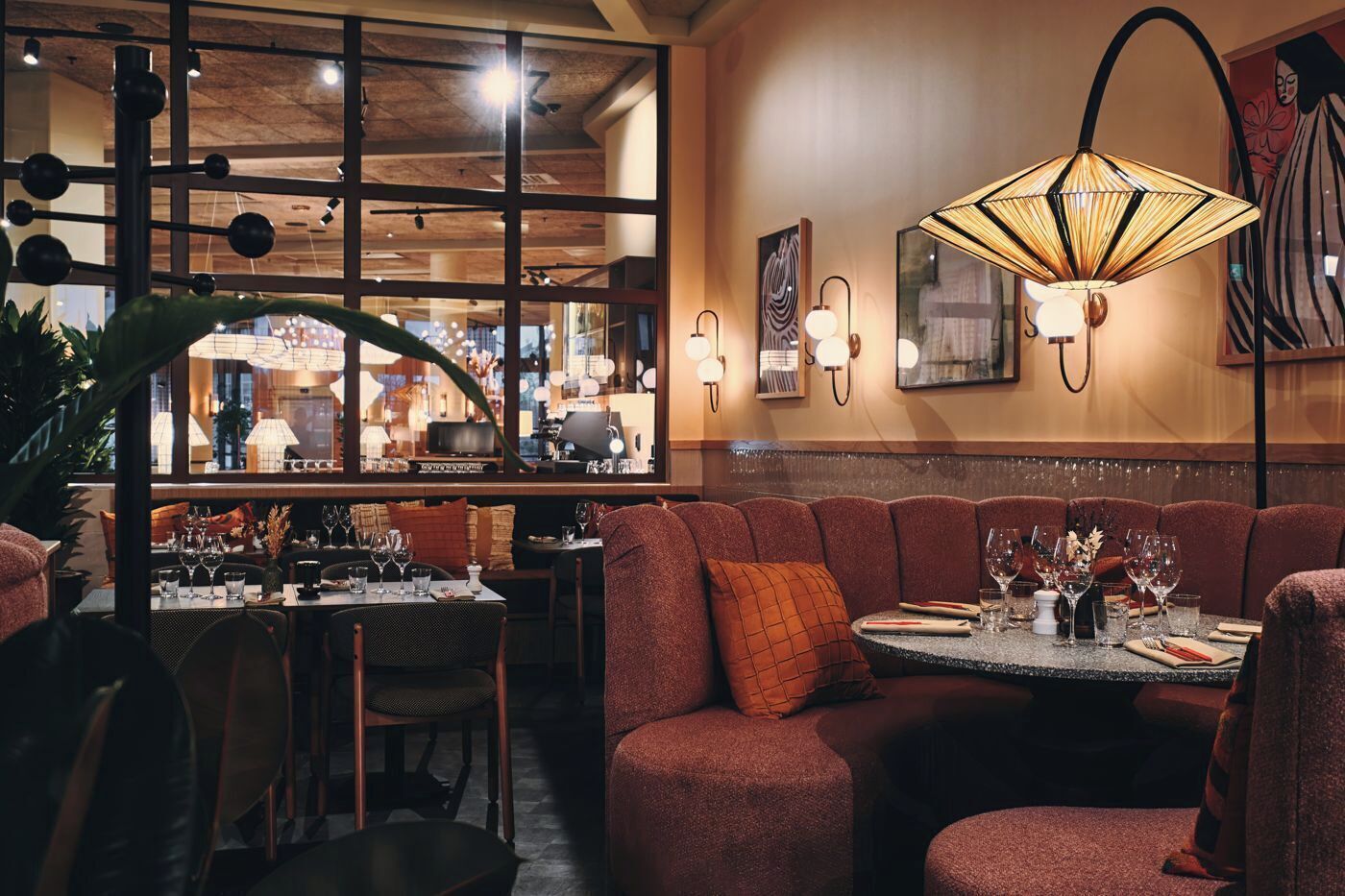 Interior acogedor de un restaurante con una zona de mesas tipo box, una mesa lista para comer y un gran ventanal con vistas a la ciudad.