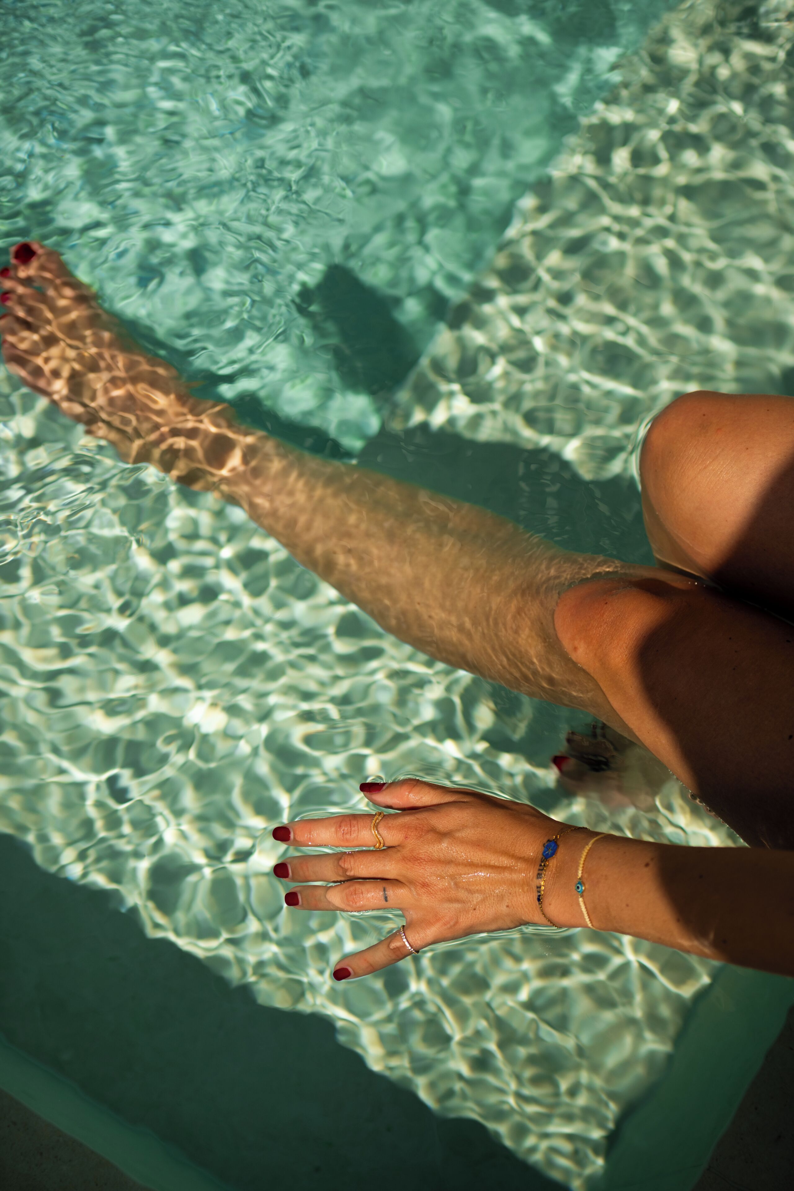 En persons ben och hand syns i klart vatten, vilket antyder att det är en pool eller något liknande vattenområde.