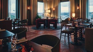 A restaurant with a view of a cityscape, featuring a mix of modern and classic furniture, a herringbone floor pattern, and ambient lighting. - The Dock (Södertälje)