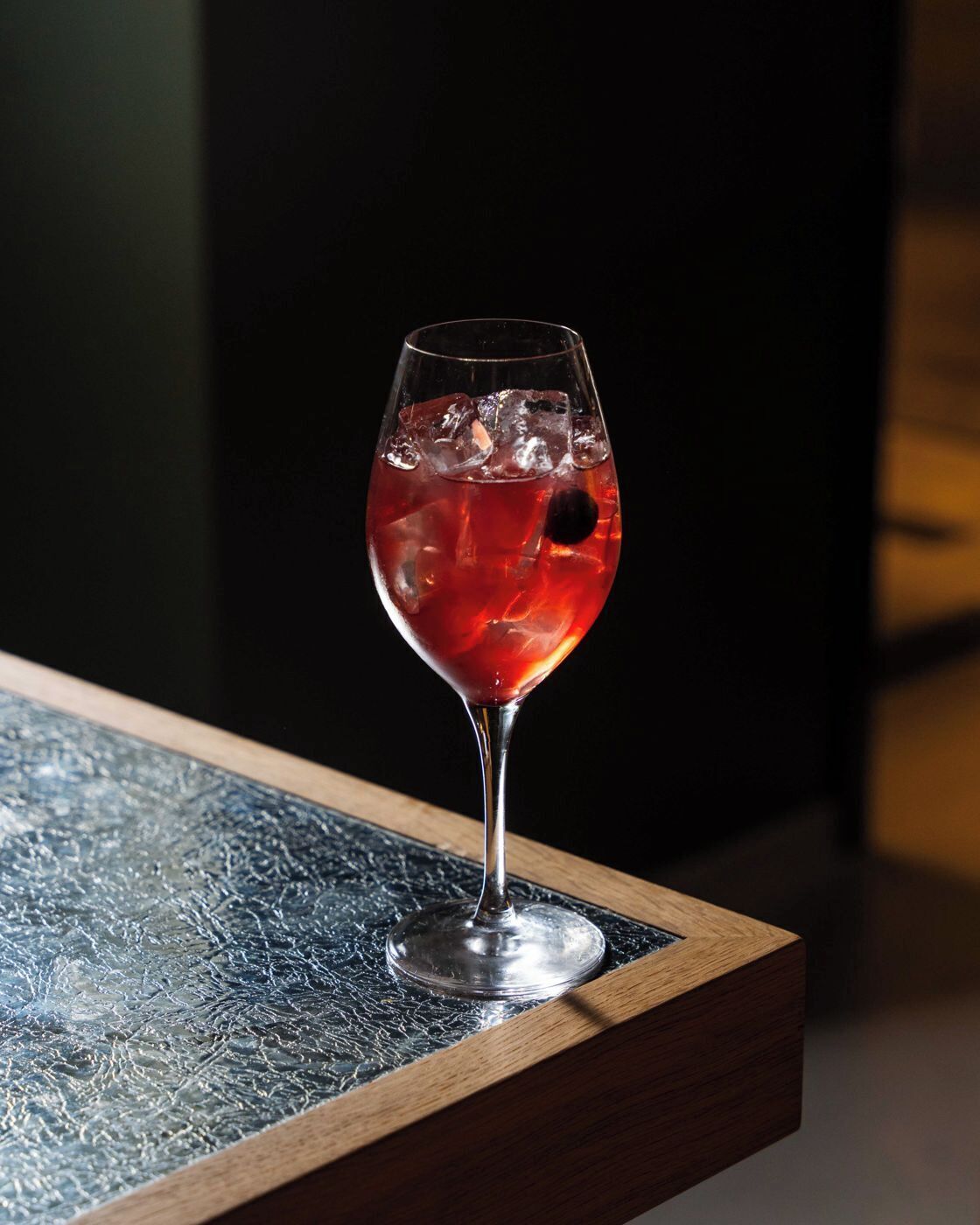 A glass of red beverage with ice cubes on a textured surface.