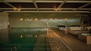 A swimming pool with a lounge area, a wall with the text 'Chill Drift Repeat,' and a ceiling with wooden beams and recessed lighting.