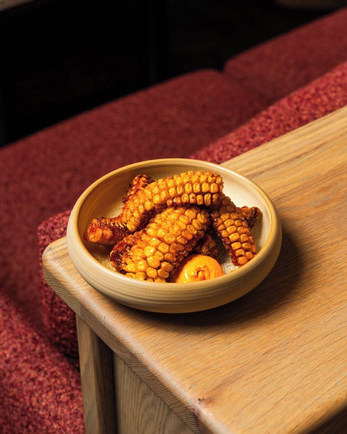 A bowl of grilled corn on the cob on a wooden table.