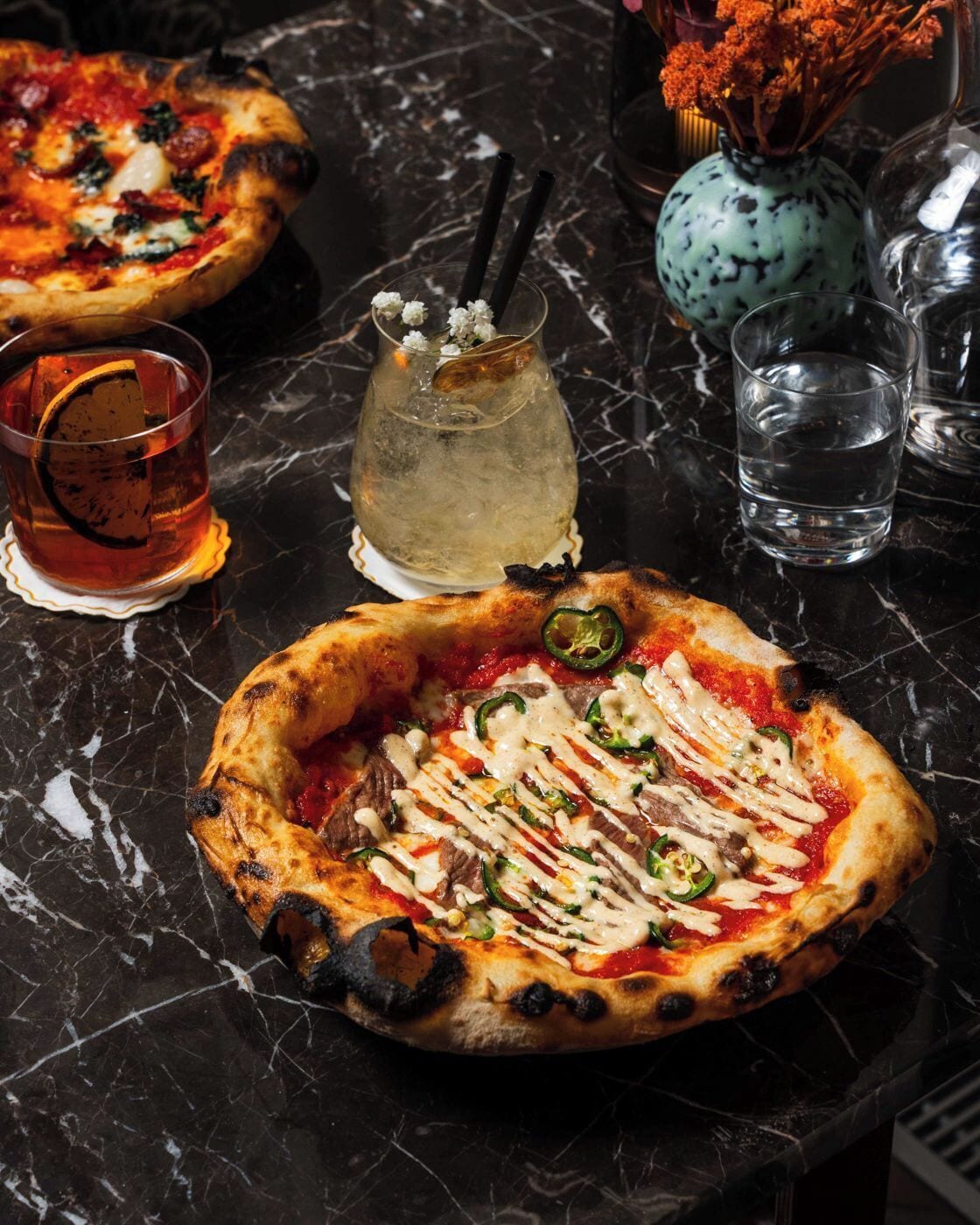Una pizza con ingredientes y una bebida sobre una mesa de mármol.
