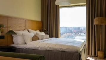 Habitación de hotel con cama, escritorio, silla, lámpara y vista a la ciudad.