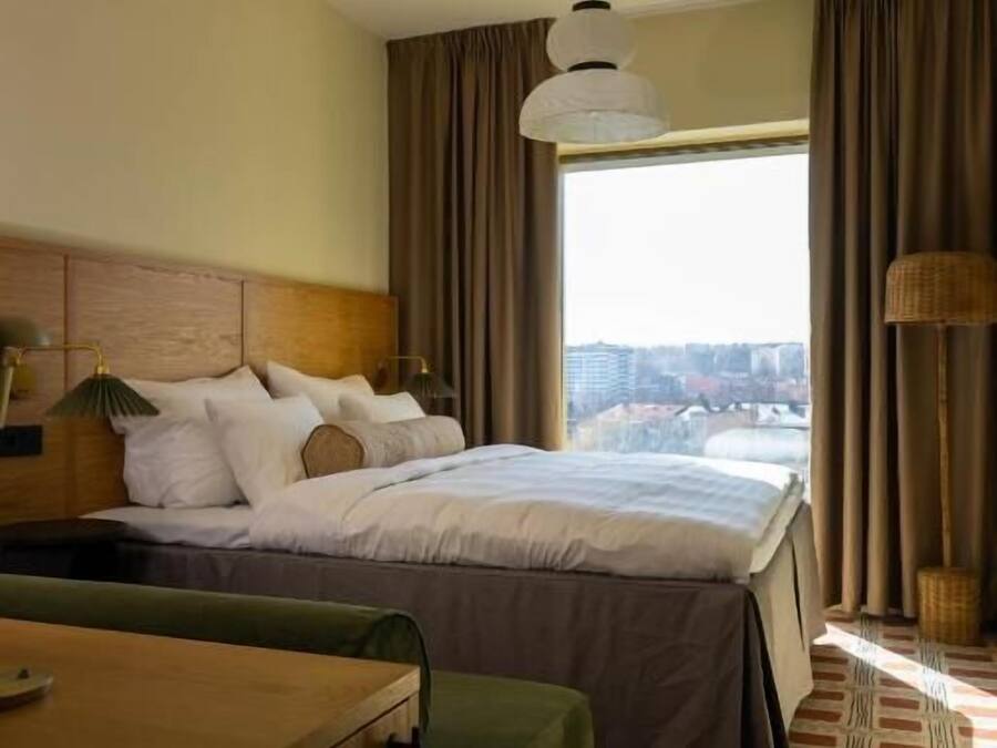 Habitación de hotel con cama, escritorio, silla, lámpara y vista a la ciudad.