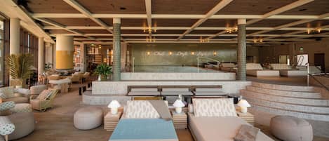 Amplio vestíbulo con zona de piscina, diversas opciones de asientos y una escalera que conduce a niveles superiores.