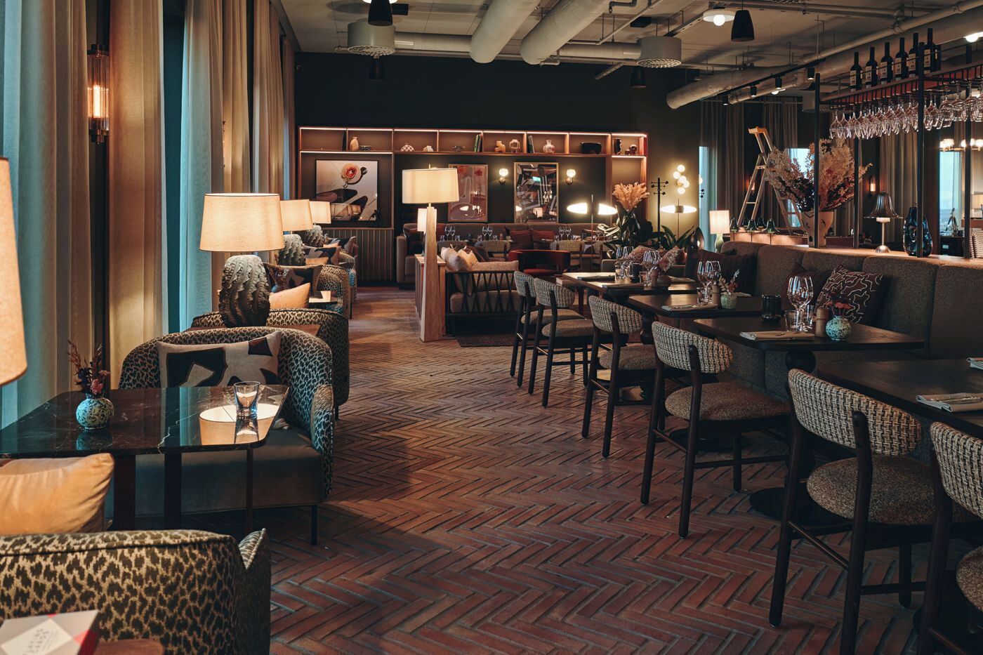 A cozy restaurant with a herringbone floor, leather sofas, and a bar area with wine glasses.