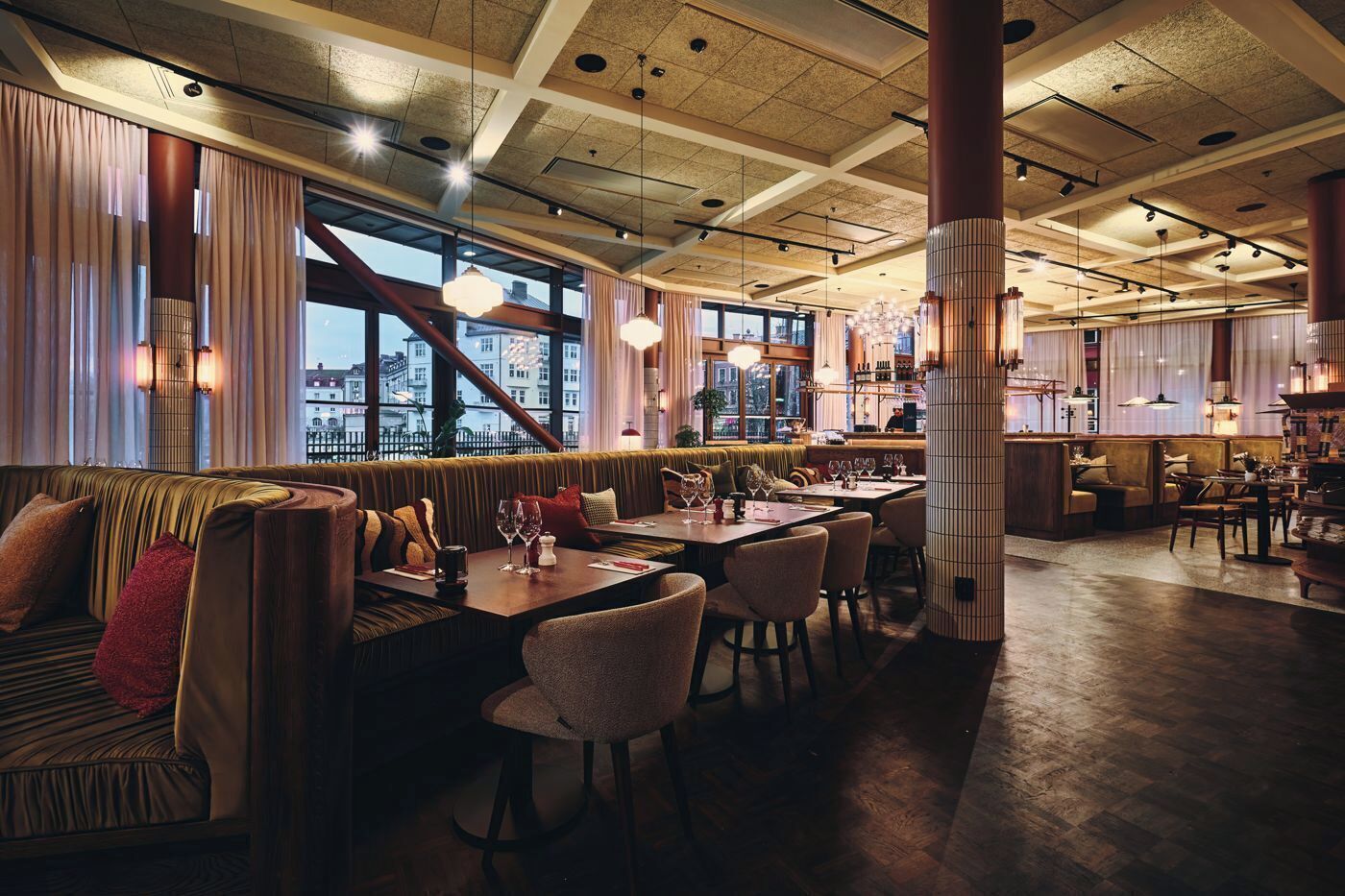A modern restaurant with high ceilings, large windows, and a cozy seating area with tables and chairs.