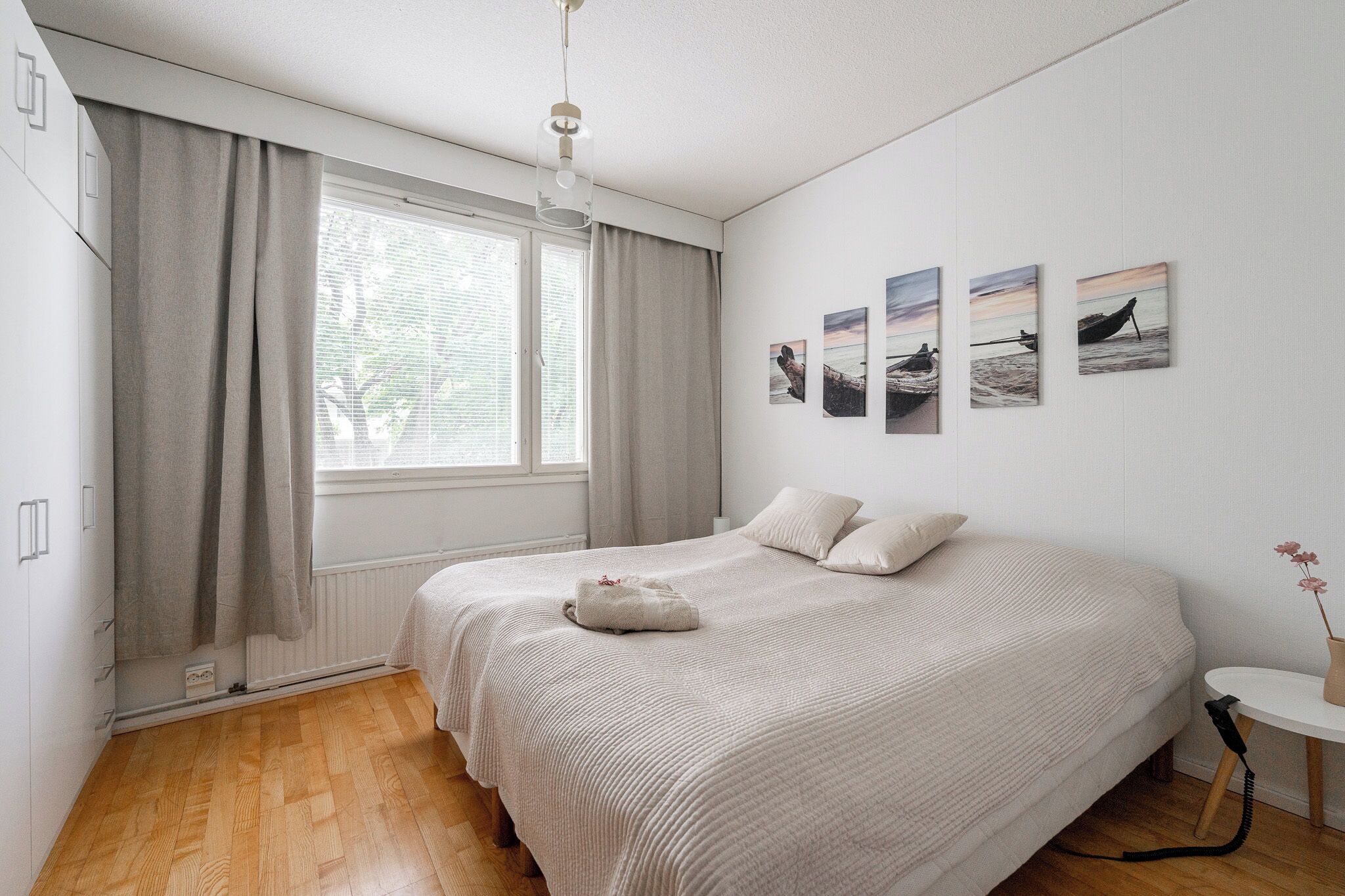 A bedroom with a large bed, a bedside table, a window with curtains, and wall art.