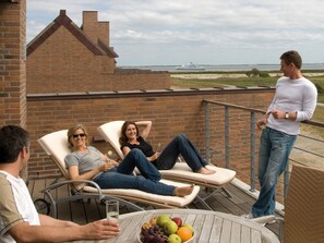 Ein Balkon mit zwei Lounge-Sesseln, einem Tisch mit Obst und Blick aufs Meer.