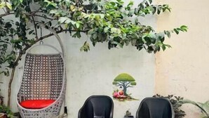 Une terrasse avec un fauteuil suspendu, deux chaises noires, une table et une fresque murale.