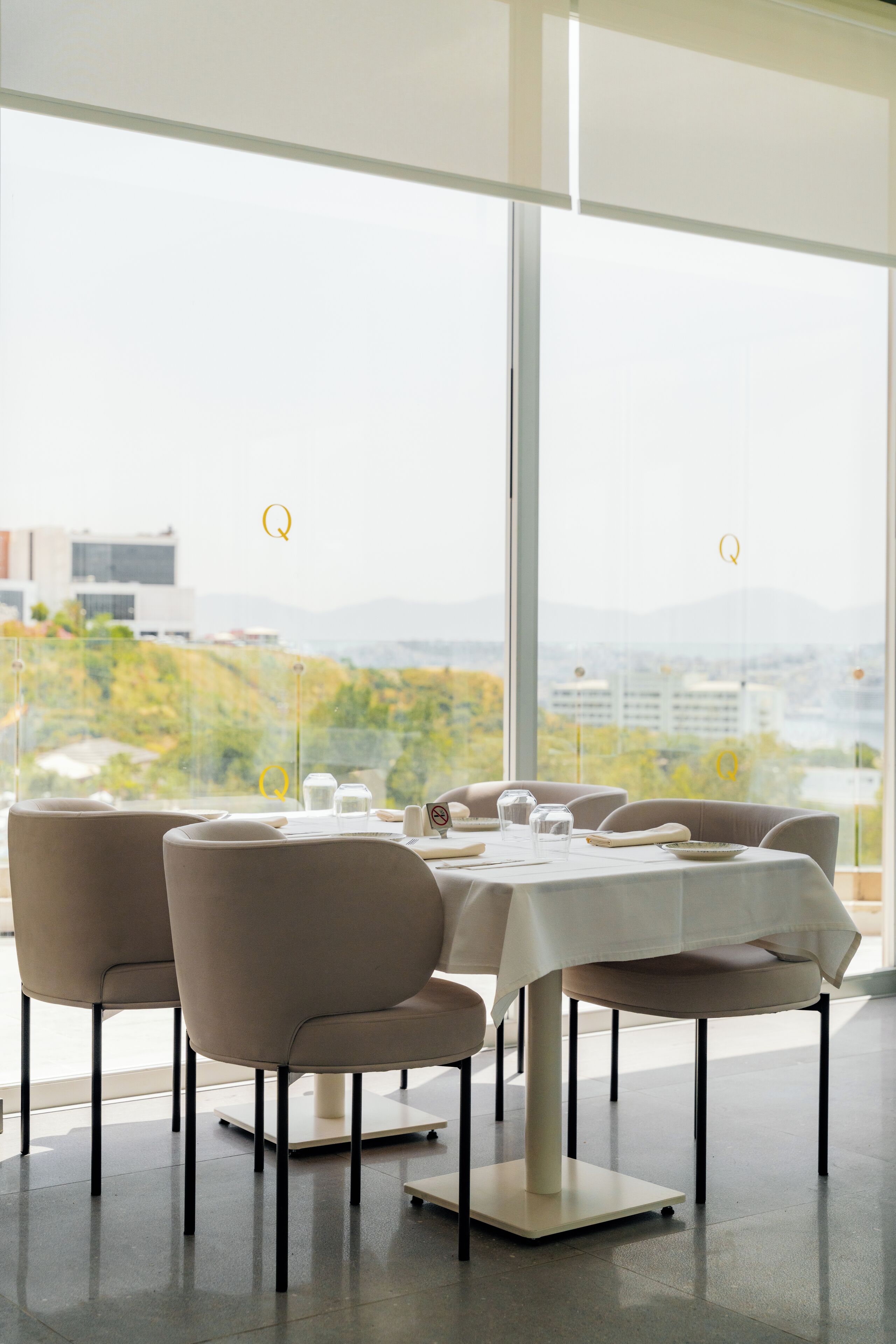 Zona pranzo con tavoli apparecchiati per quattro, ampie finestre che offrono vista su una città e aree verdi.