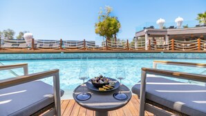 A poolside dining area with a table set for two, two wine glasses, and a bowl of fruit. - Qlusive Hotel (Kusadasi)