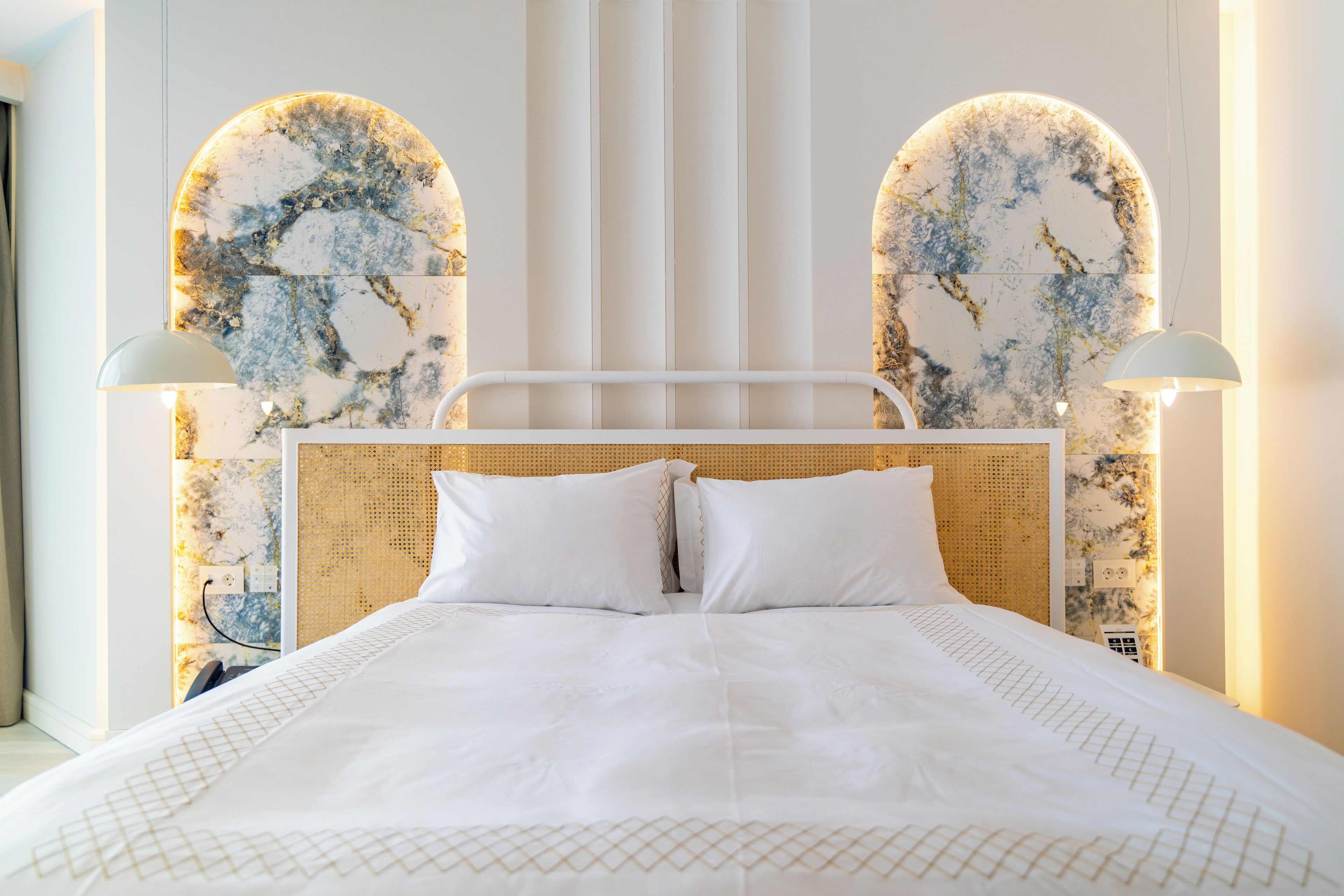A neatly made bed with a white comforter and pillows, a white metal headboard, and two wall sconces.