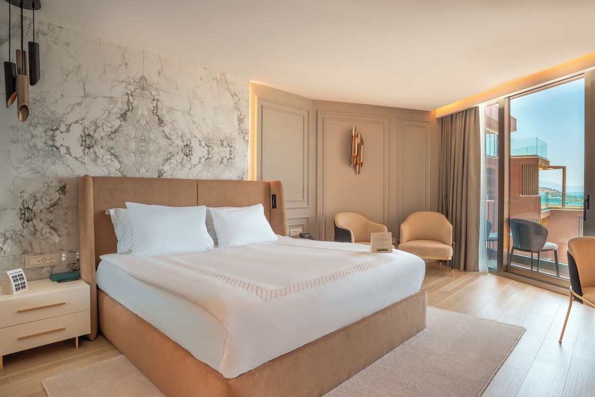 A modern hotel room with a large bed, a desk, a chair, and a view of the sea.