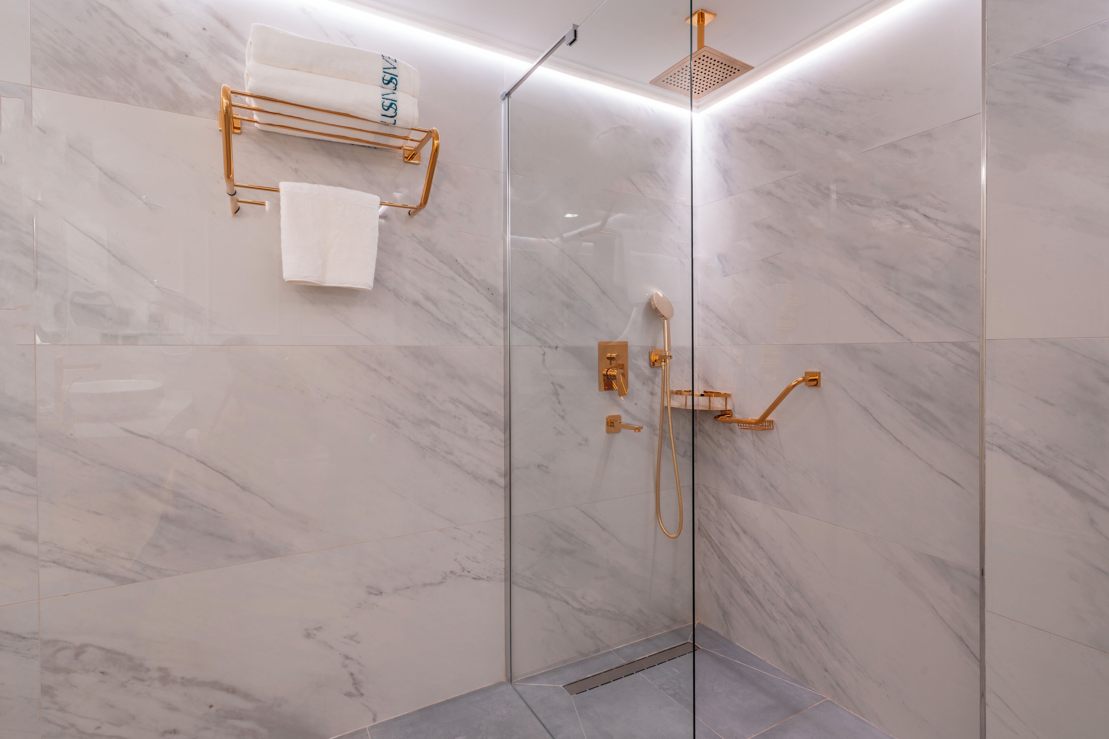 Una ducha moderna con cabina de vidrio, paredes de mármol y accesorios dorados.