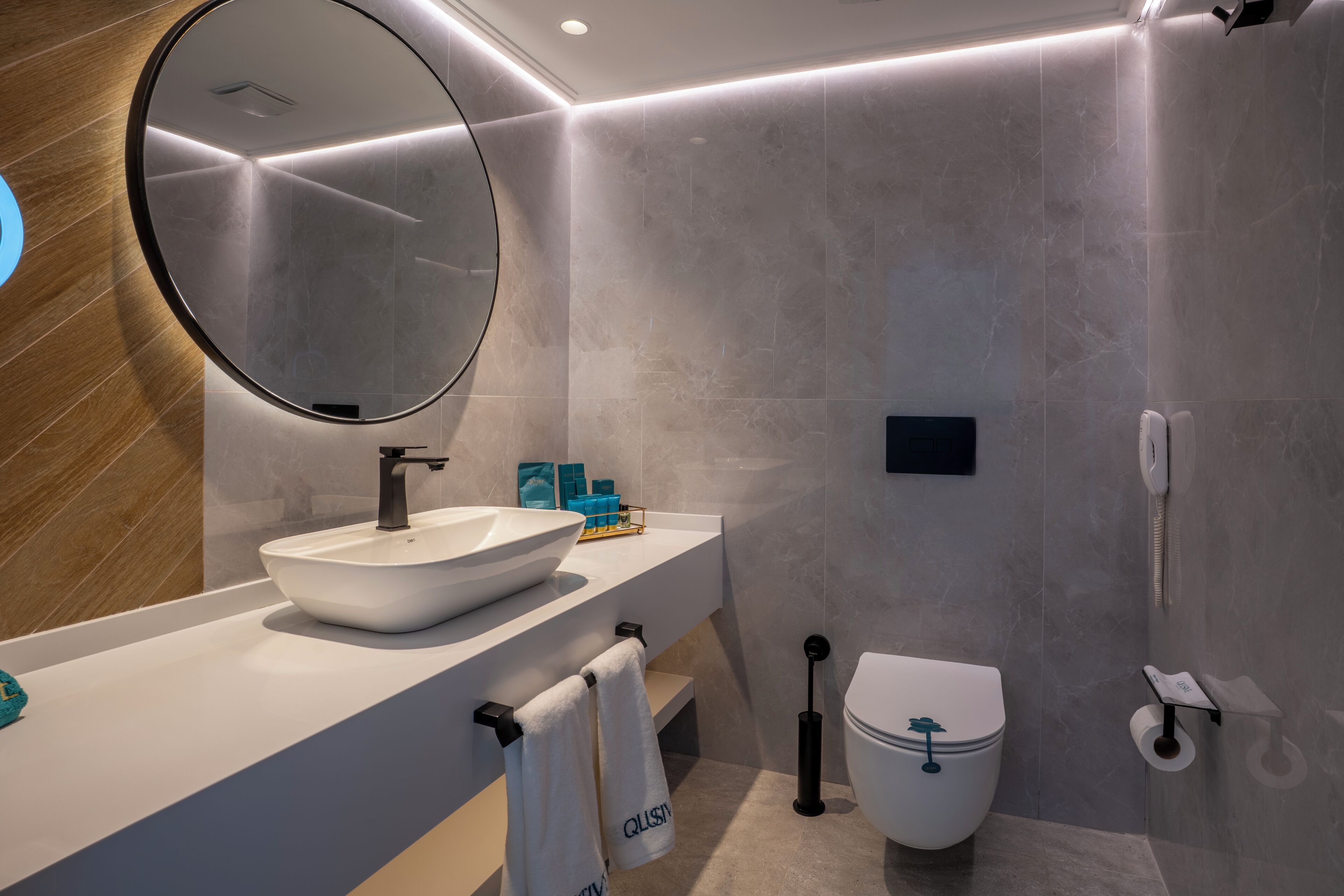 Une salle de bain moderne avec un miroir rond, un lavabo blanc et des toilettes.