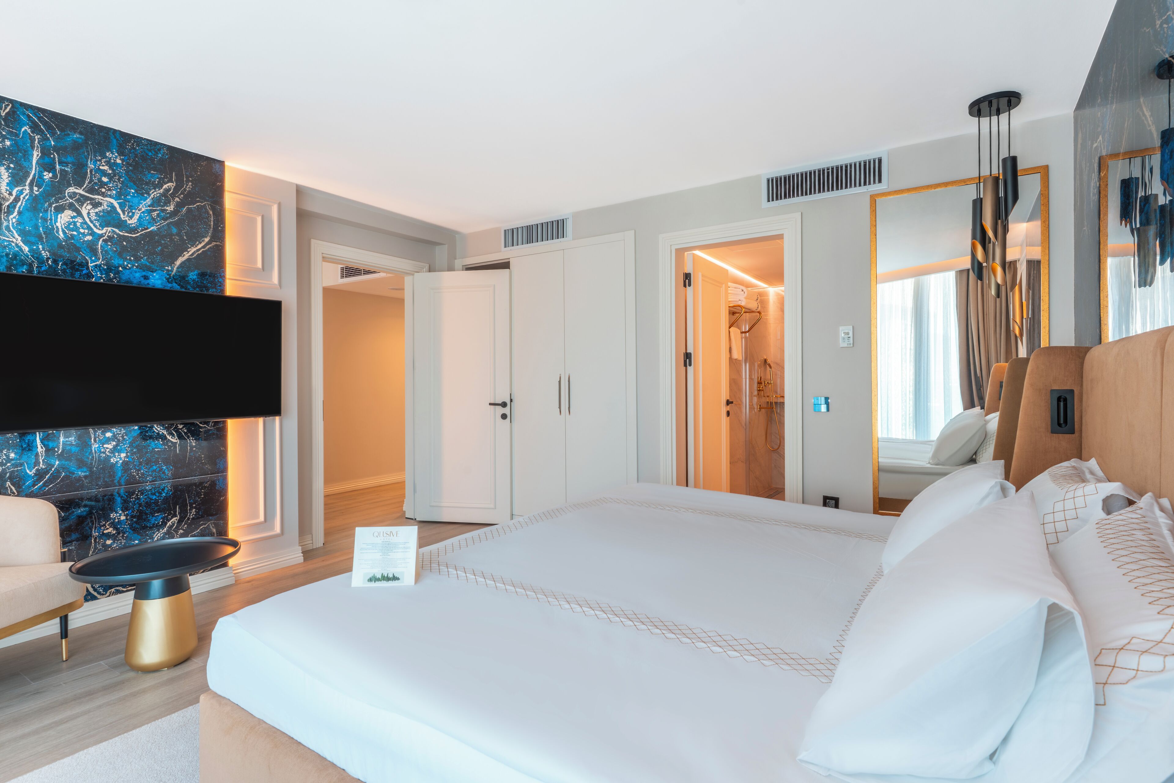 Une chambre d’hôtel moderne dotée d’un grand lit, d’un téléviseur à écran plat, d’un coin salon et d’une salle de bain visible à travers une porte ouverte.