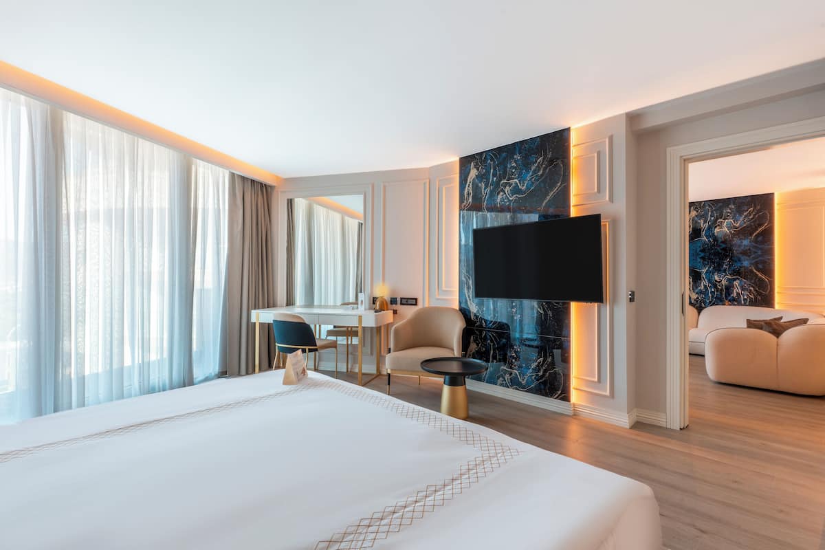 A modern hotel room with a large bed, a desk, a chair, and a TV.