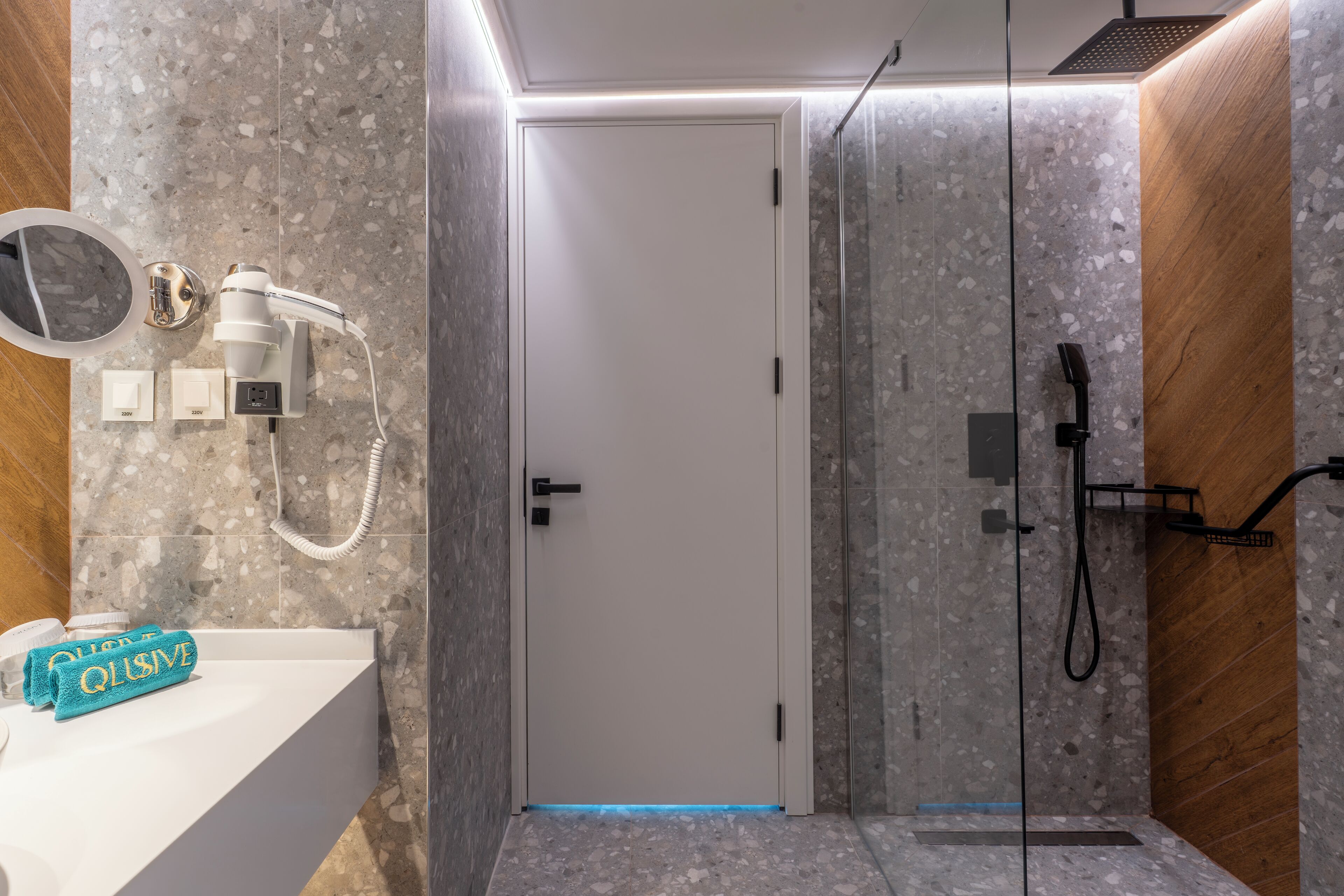 Une salle de bain moderne avec un pare-baignoire en marbre, un lavabo blanc, une serviette et un espace douche.