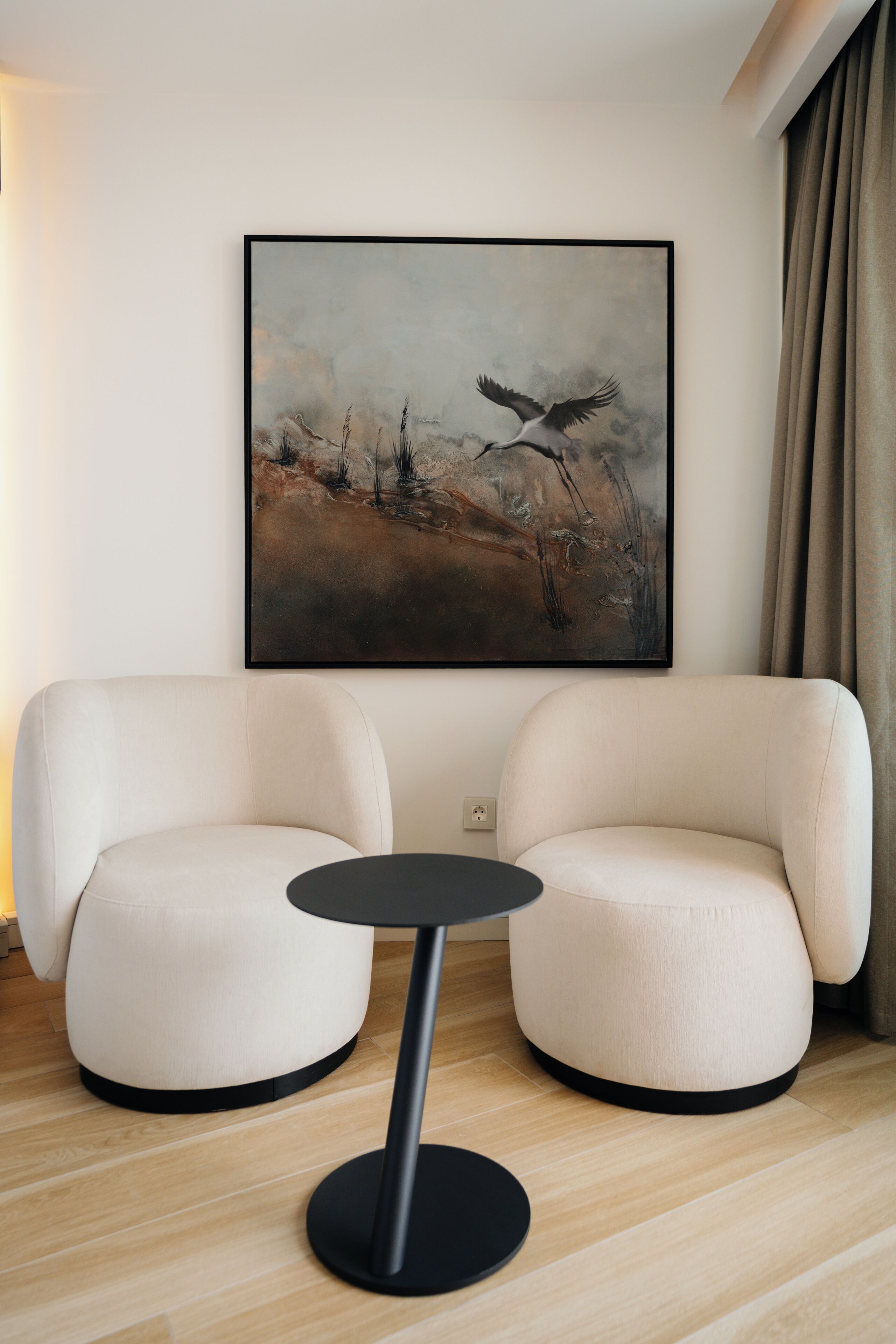 A modern living room with two white armchairs, a small black table, and a framed abstract painting on the wall.