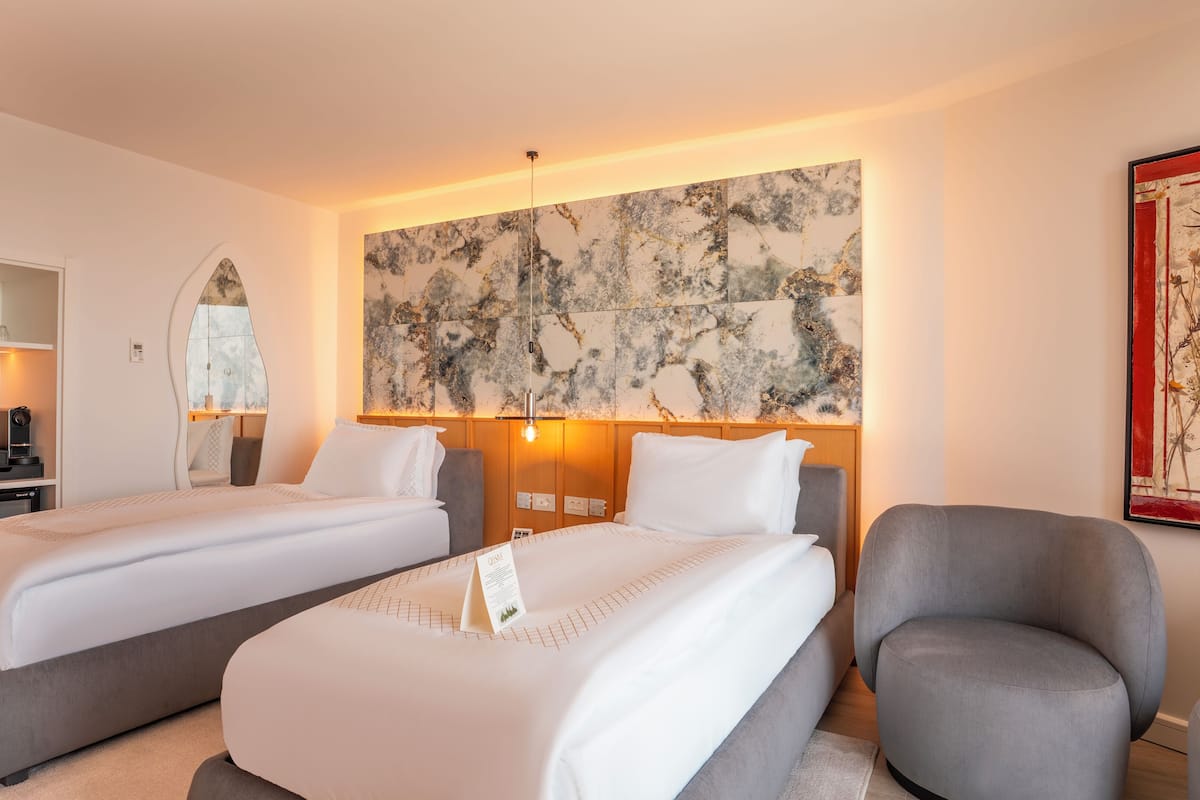 A hotel room with two beds, a desk with a computer, a mirror, and a large abstract painting on the wall.