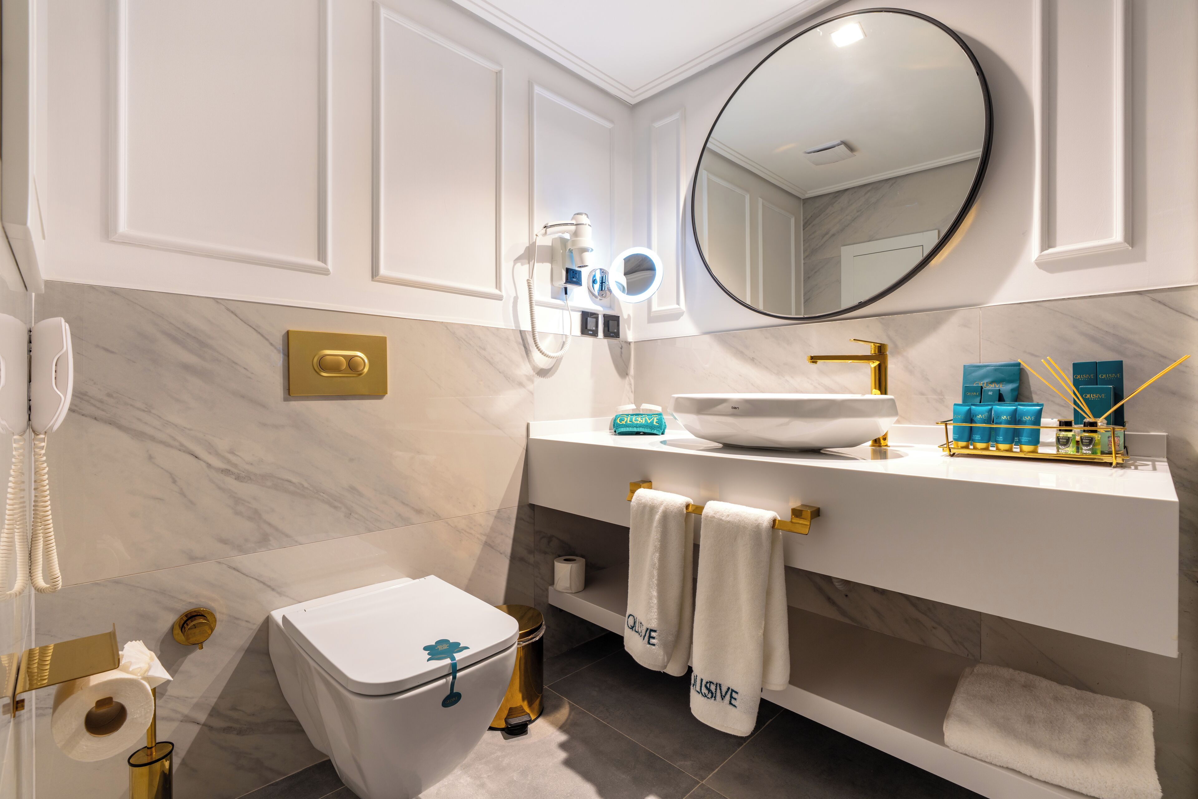 A modern bathroom with a toilet, bidet, vanity, and a large mirror.