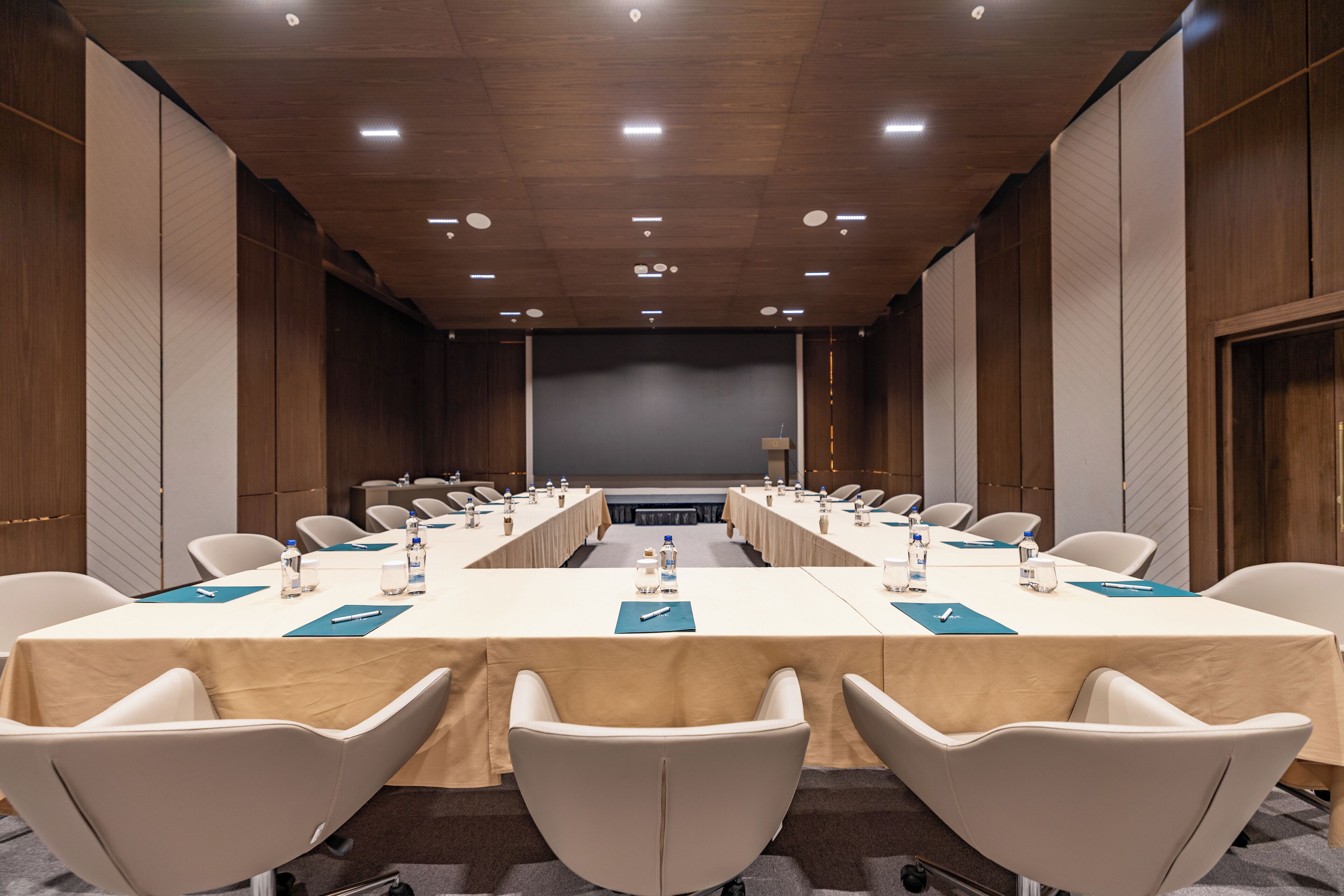 A conference room with a long table, multiple chairs, and a stage at the front.