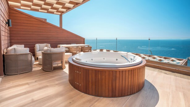 A wooden deck with a hot tub, wicker furniture, and a clear view of the ocean. - Qlusive Hotel (Kusadasi)