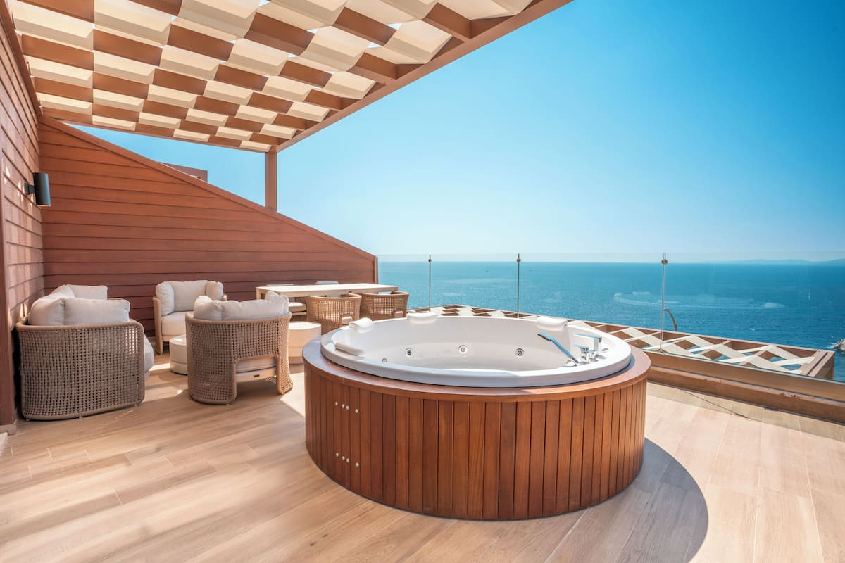 A wooden deck with a hot tub, wicker furniture, and a clear view of the ocean.