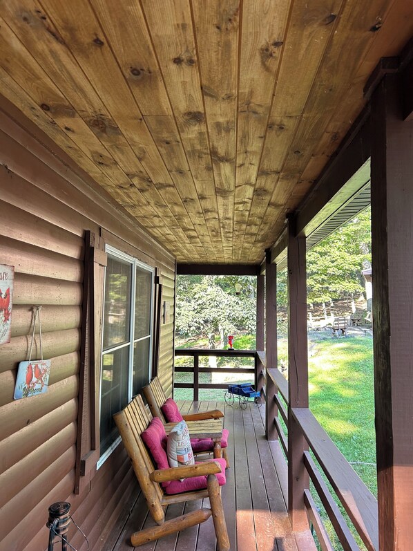 A wooden porch with two rocking chairs, a small table, and a window.
