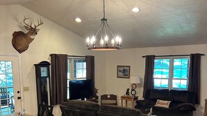 Ein modernes Wohnzimmer mit einem großen, dunkelbraunen Sofa, einem Holzesstisch, einer Küchenzeile mit integriertem Kochinsel und einem Deckenventilator.