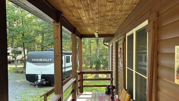 Eine überdachte Veranda mit hölzernen Bänken und Blick auf einen Campingplatz.